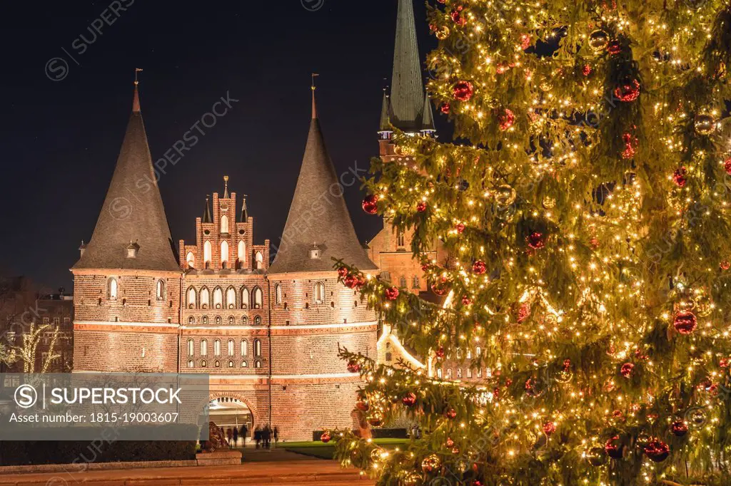 Germany, Schleswig-Holstein, Lubeck, Illuminated¶ÿHolstentor gate at night with glowing Christmas tree in foreground