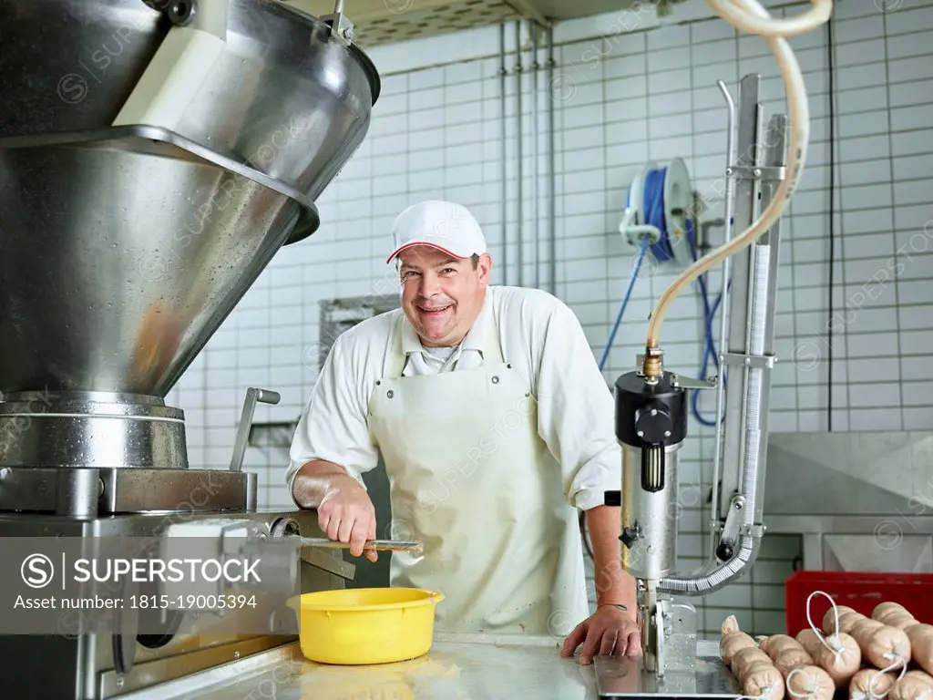 Happy butcher standing by machinery in factory