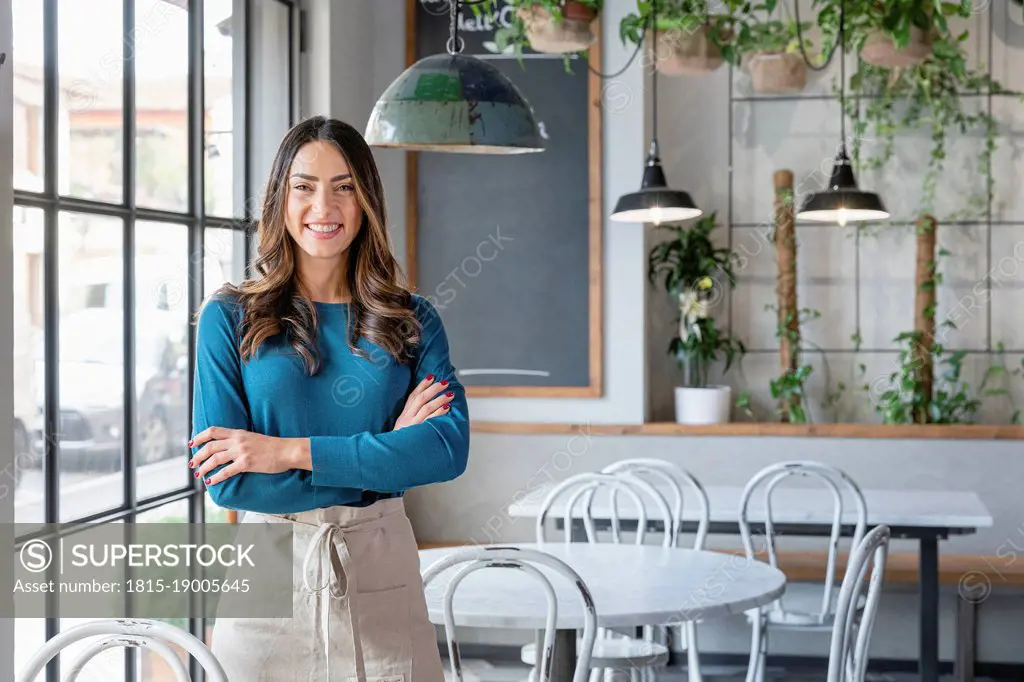 Smiling woman standing with arms crossed in cafe