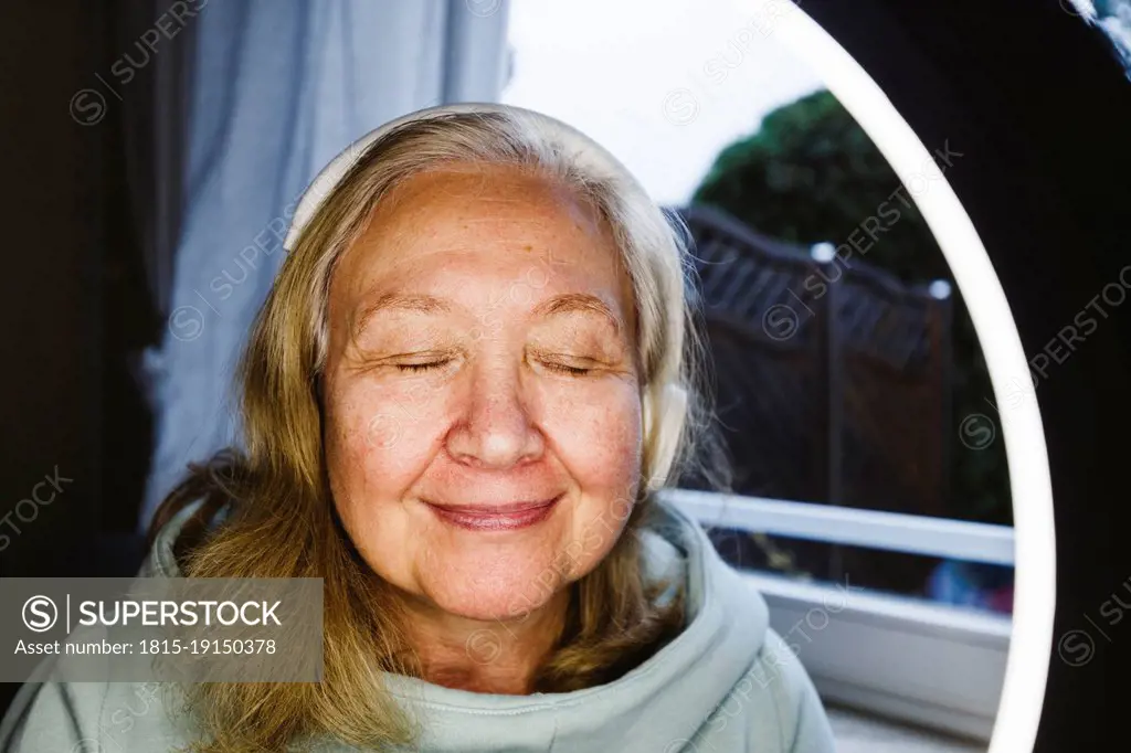 Senior woman with eyes closed seen through illuminated ring light