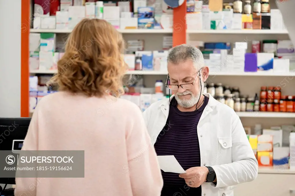 Pharmacist reading prescription standing with customer at checkout counter in pharmacy store