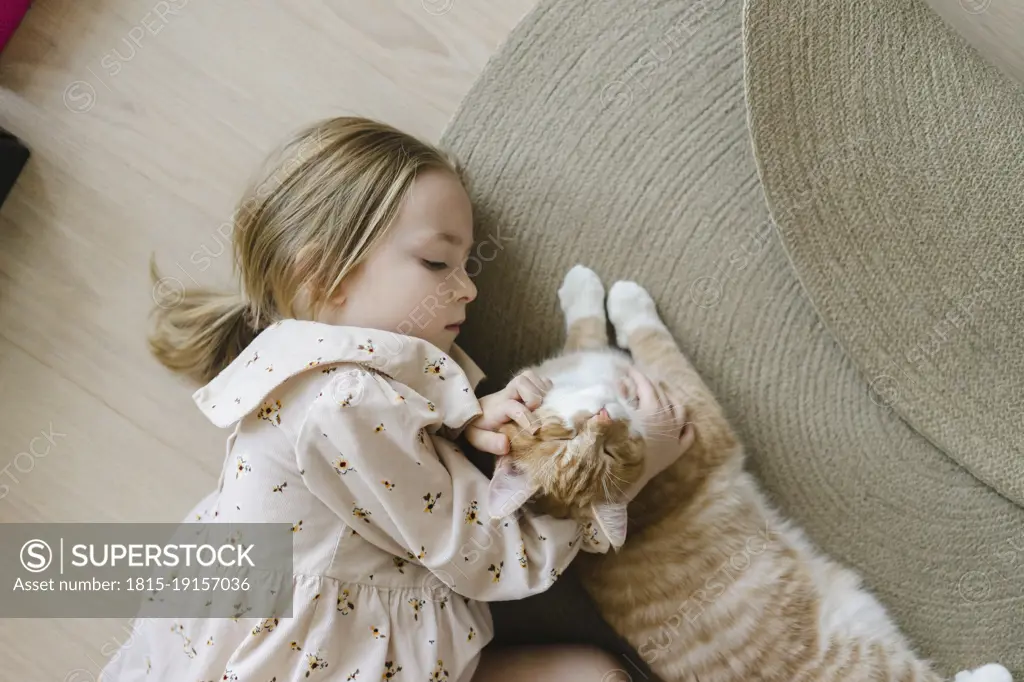 Blond girl stroking cat lying on floor at home