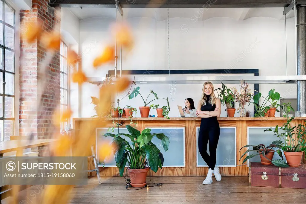 Businesswoman with arms crossed standing by potted plants in living room at home