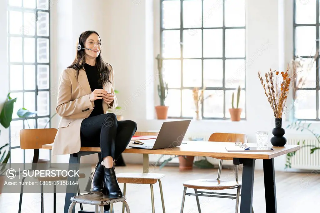 Smiling businesswoman talking through headset sitting on table at home office