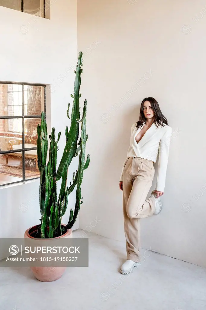Woman leaning on white wall by potted plant at home