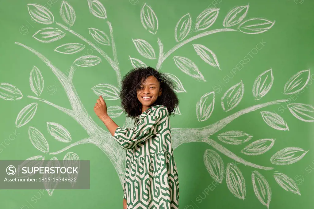 Smiling woman standing in front of tree drawing on green wall