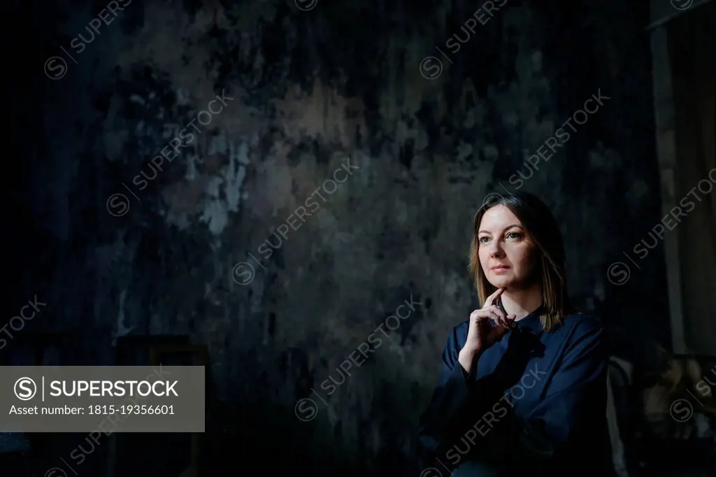 Thoughtful woman sitting with hand on chin against wall