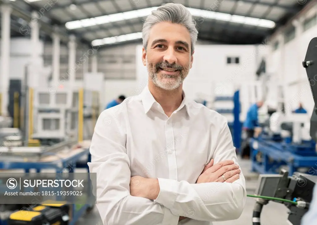 Smiling businessman standing with arms crossed in factory