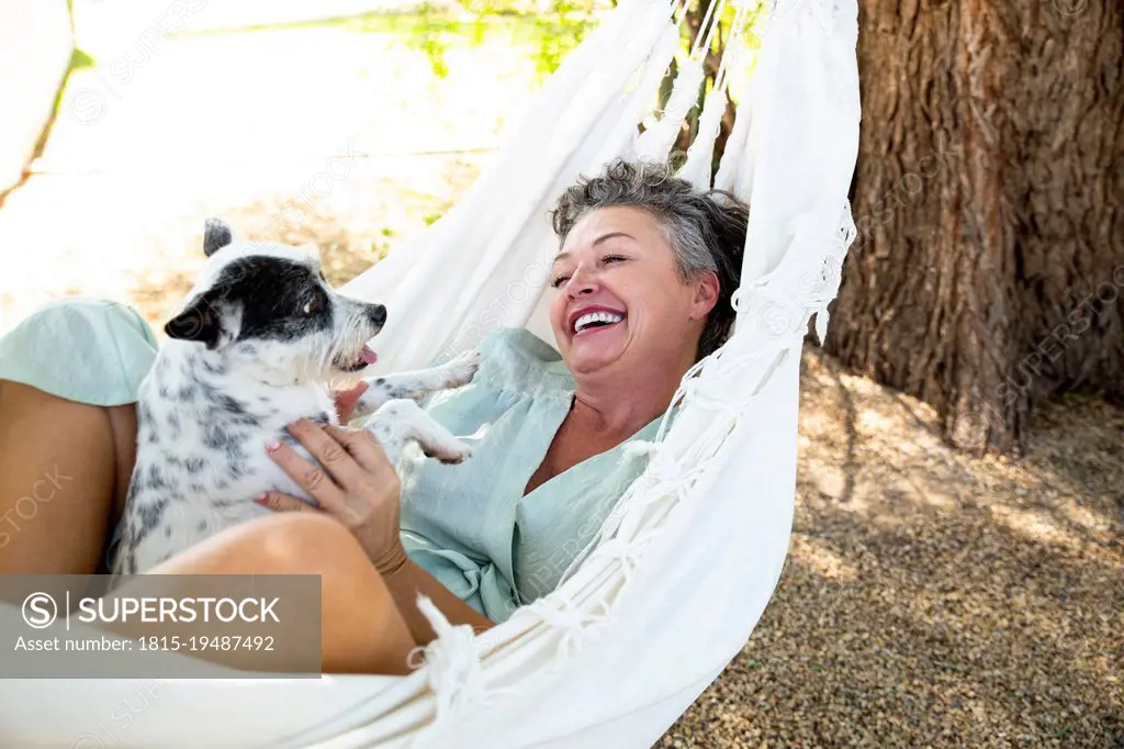 Happy woman with pet dog lying in hammock