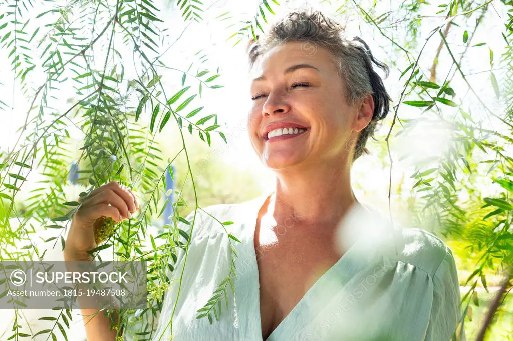 Smiling woman with eyes closed standing amidst twigs in garden