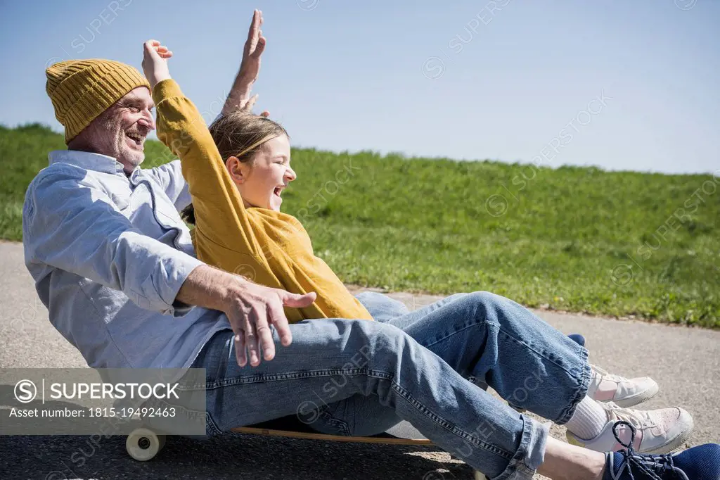 Playful senior man enjoying skateboarding with granddaughter on road