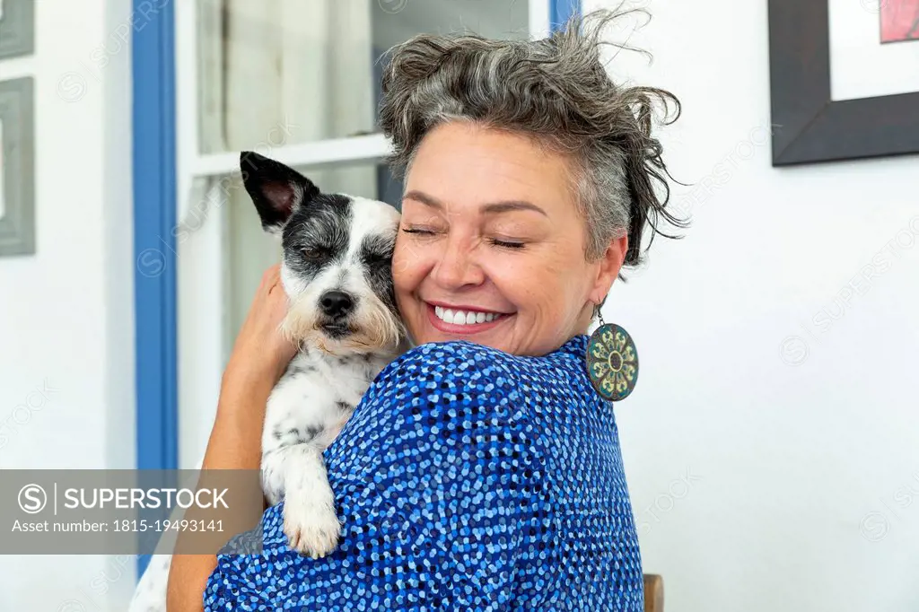 Happy mature woman with short hair embracing dog at home