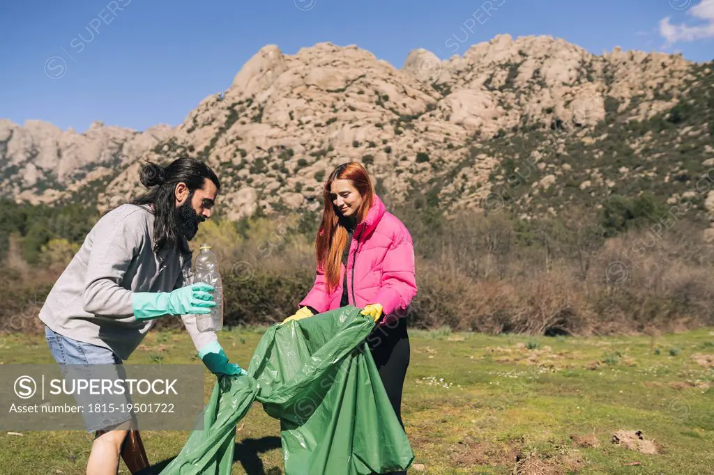 Man and woman with garbage bag collecting plastic bottle on sunny day