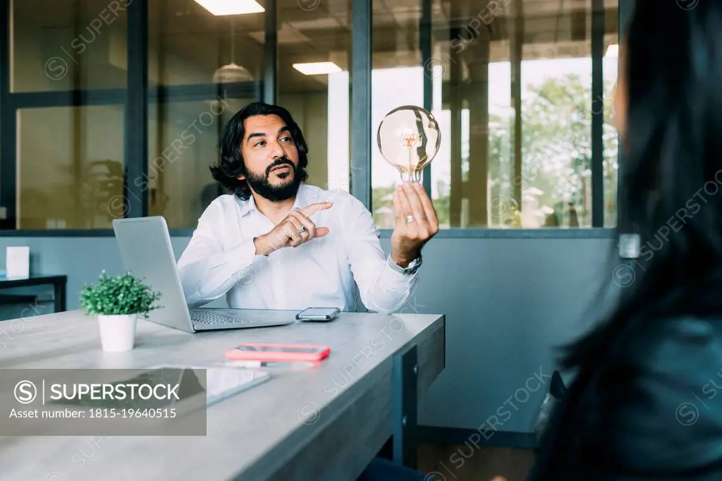Businessman discussing over light bulb with colleague at work place