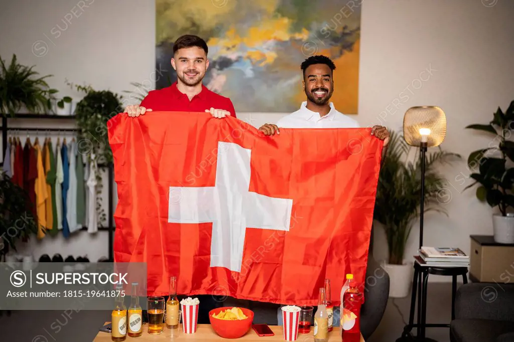 Happy football fans standing with Swiss flag at home