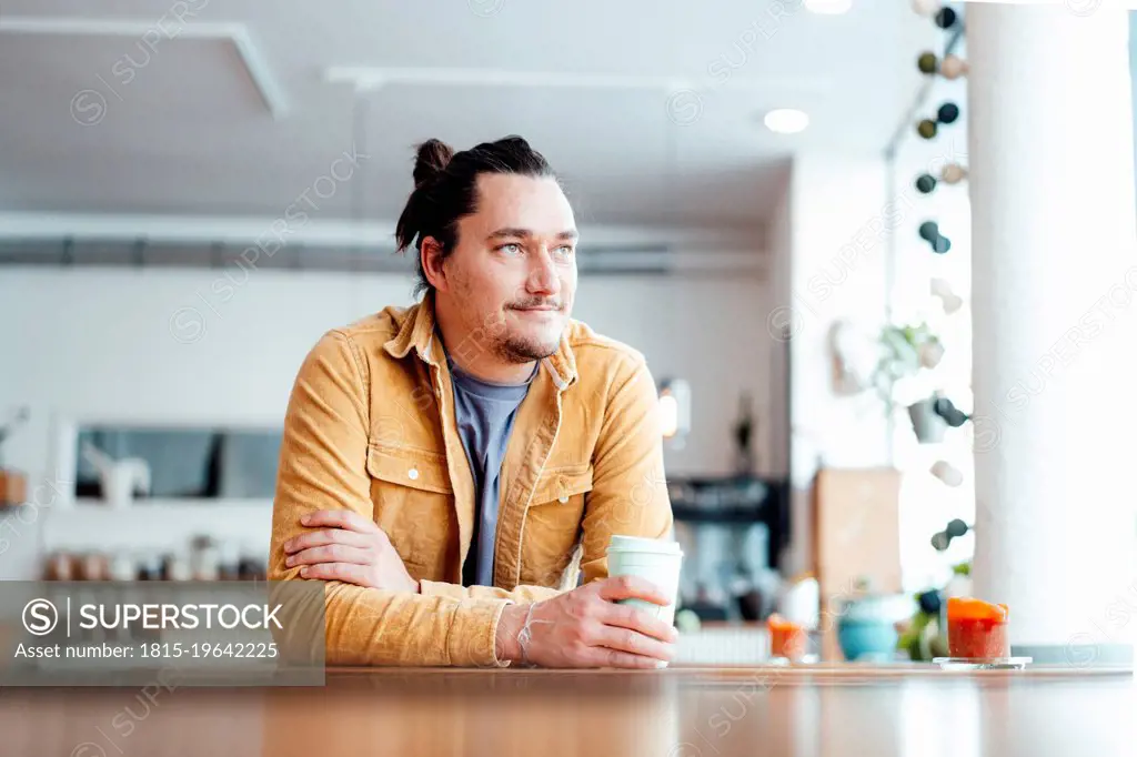 Smiling man with disposable coffee cup sitting at table in cafe