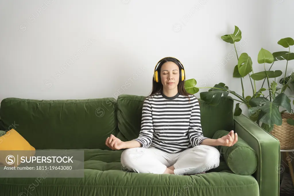 Woman listening music and meditating on sofa at home