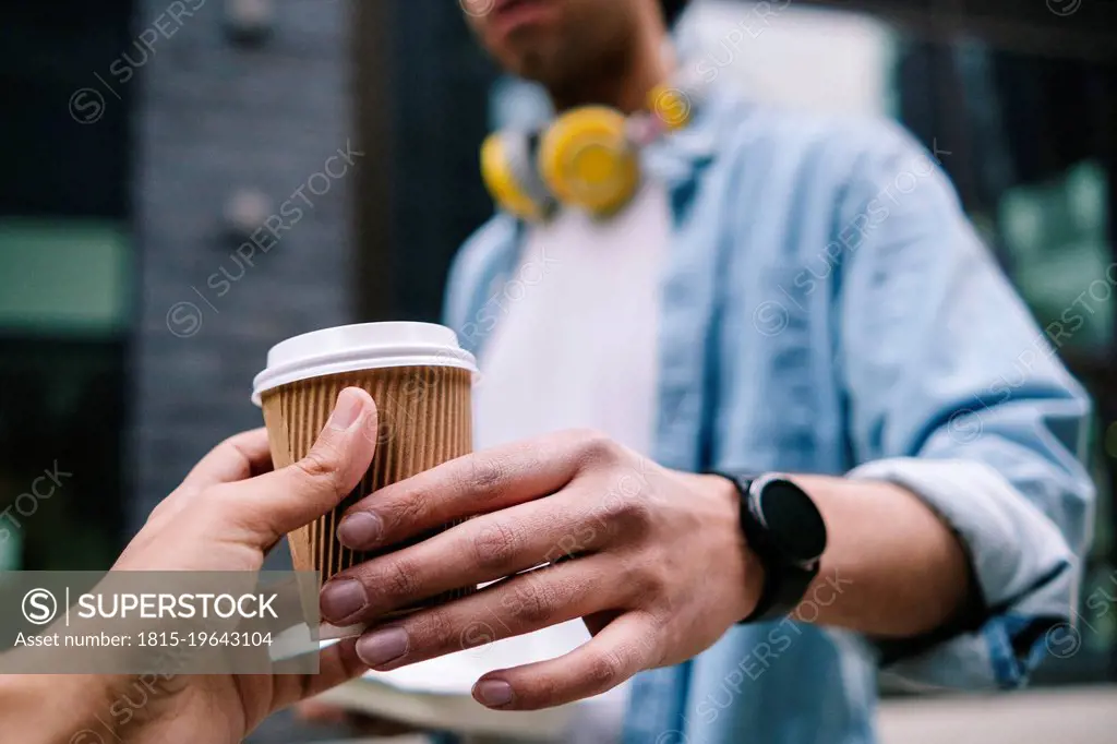 Man passing disposable drink cup to friend