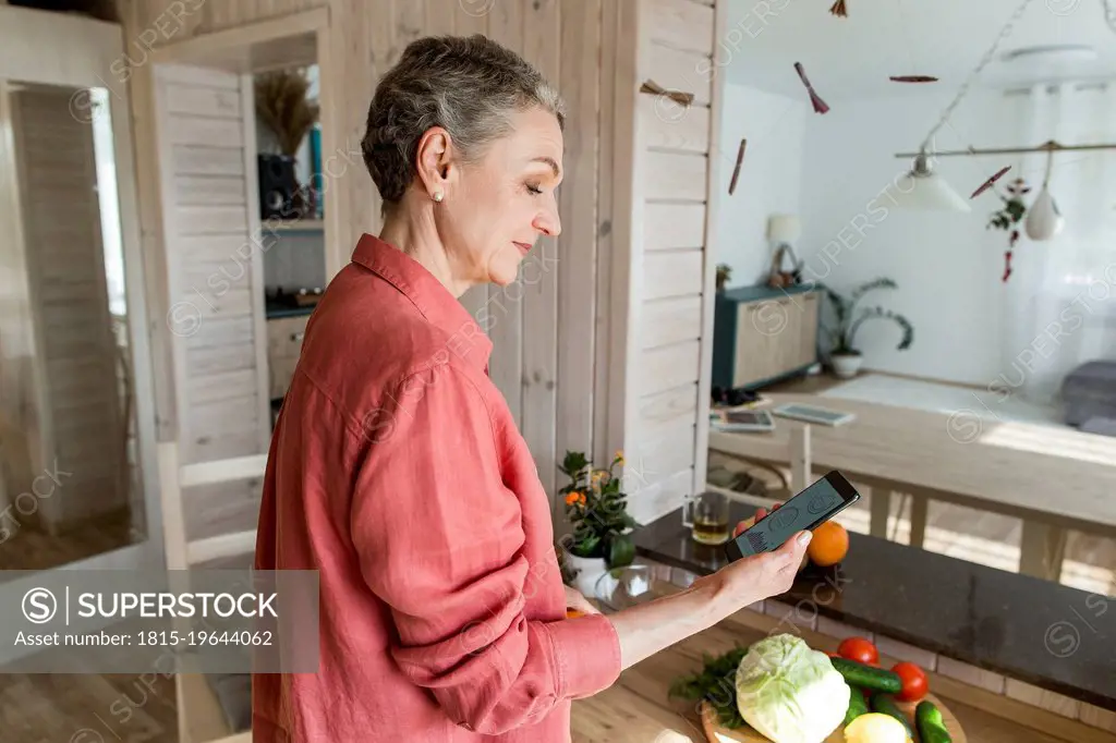 Woman in kitchen at home holding smartphone