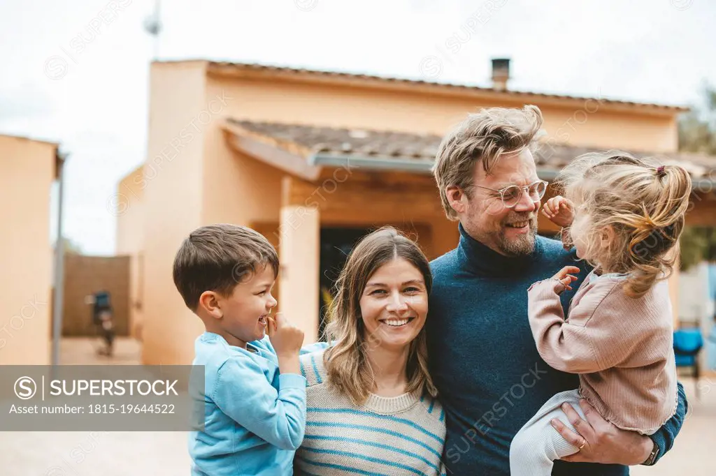 Happy parents carrying children in front of house