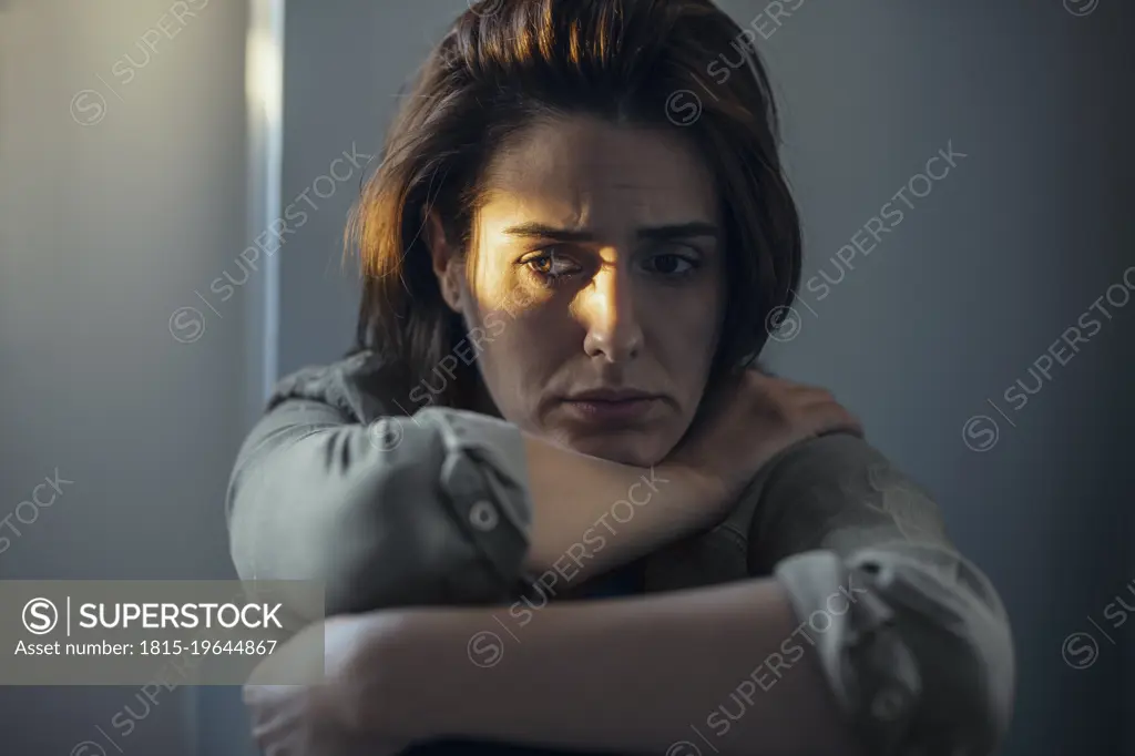 Worried woman sitting with sunlight on face at home