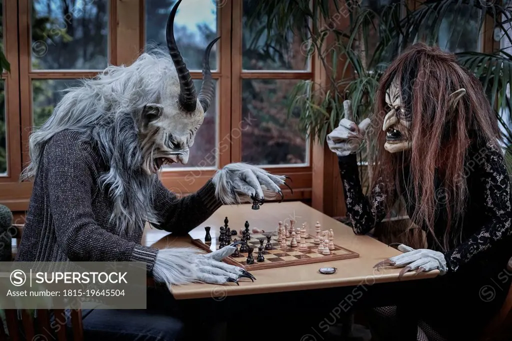 Mature man and woman in ghost costume playing chess game sitting at table