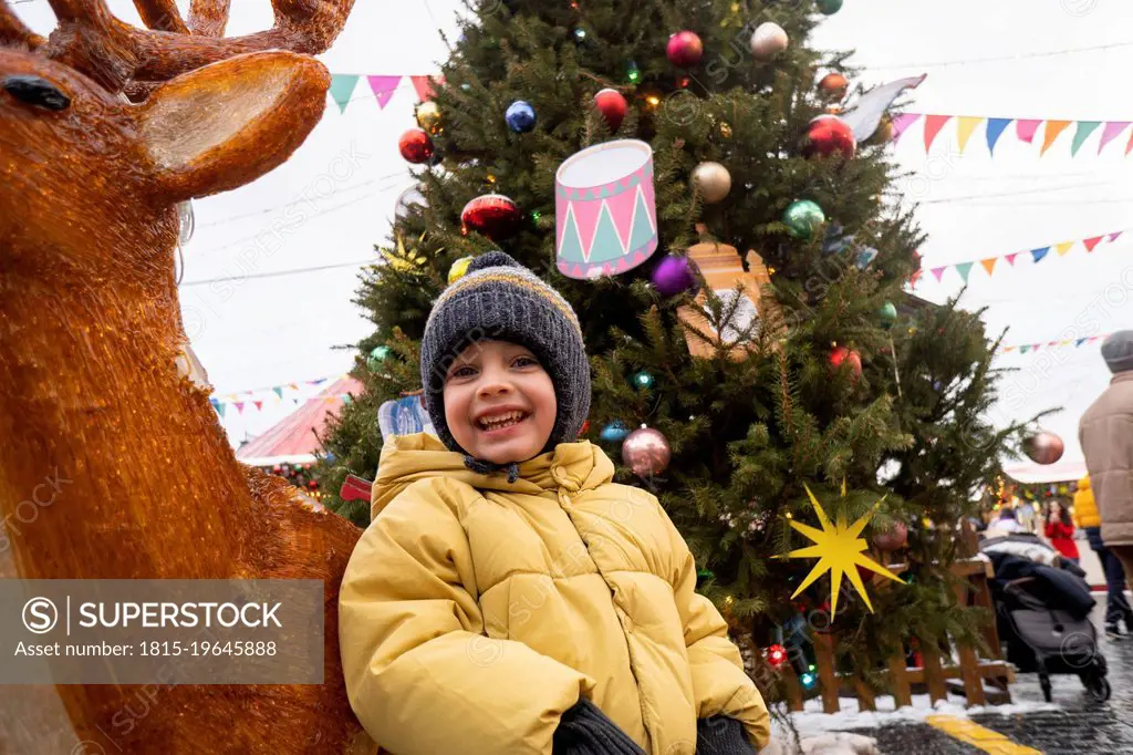 Happy boy standing by deer decoration at Christmas market