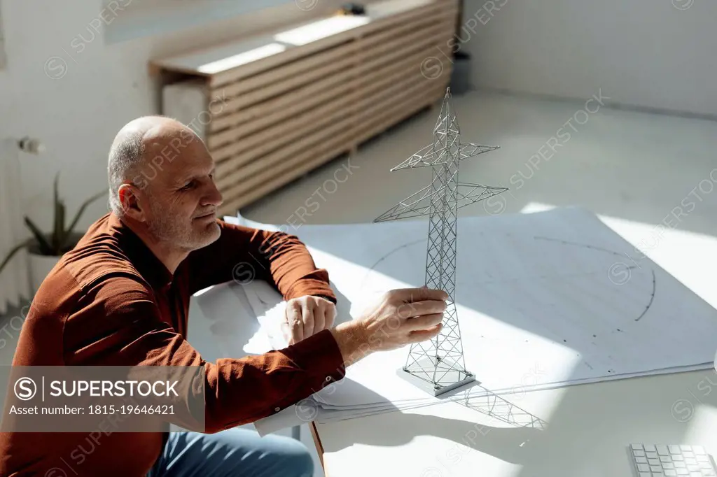 Businessman examining electricity pylon model on blueprint at desk