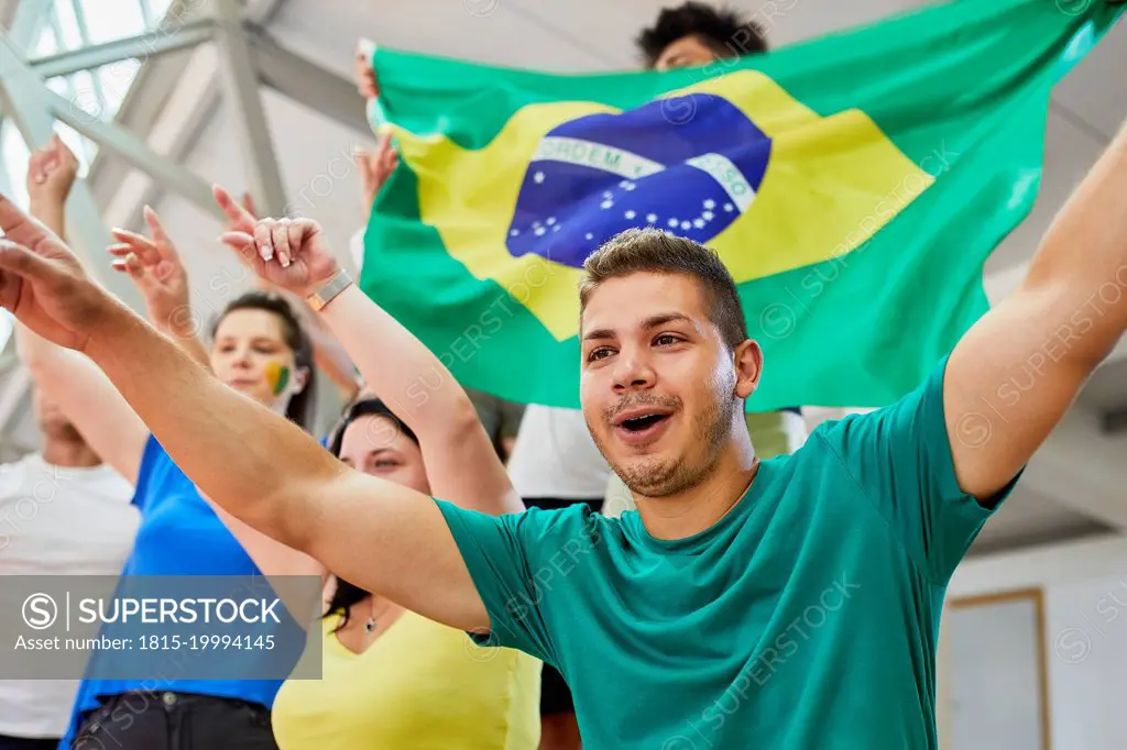 Man with arms raised cheering with fans at sports event in stadium