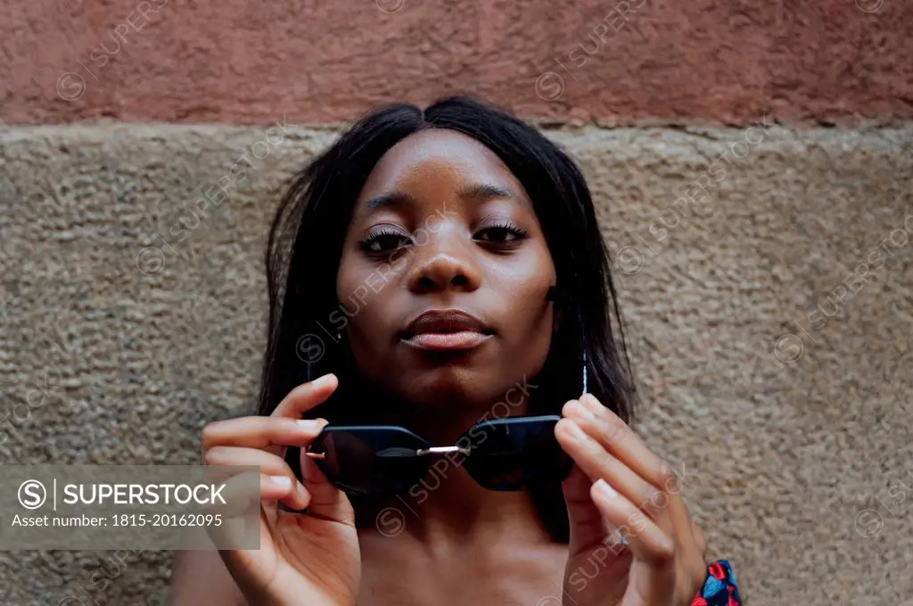 Young woman wearing sunglasses in front of wall