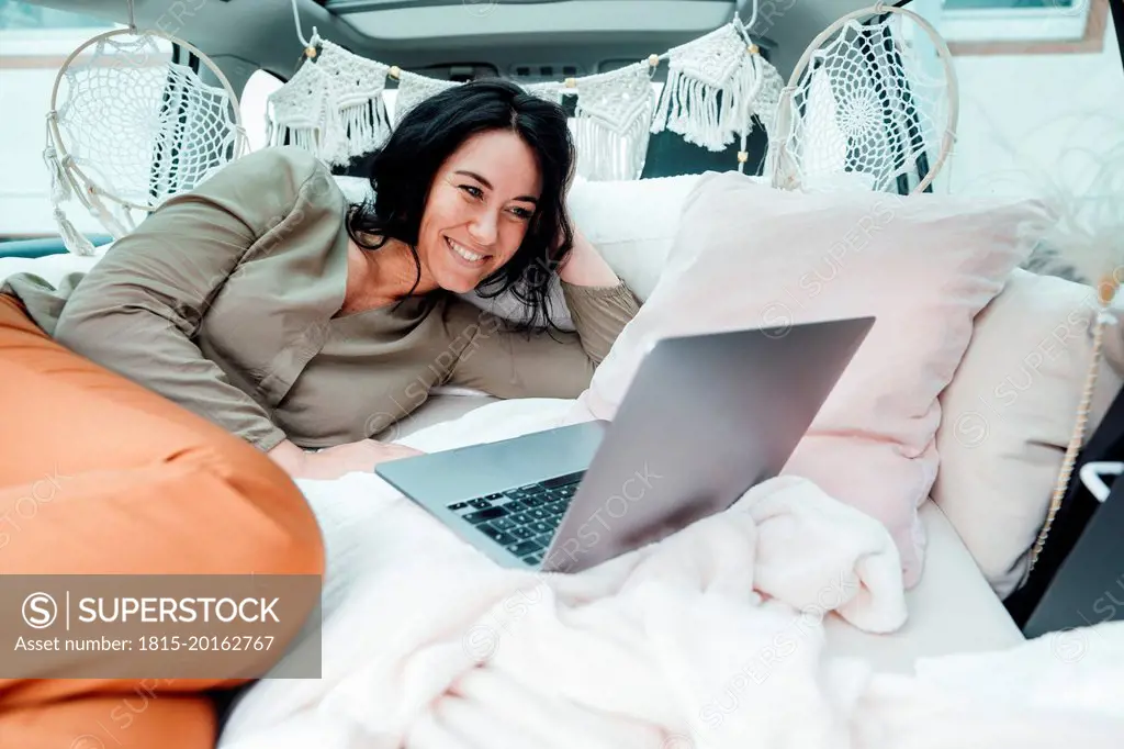 Happy woman watching movie on laptop lying in car trunk