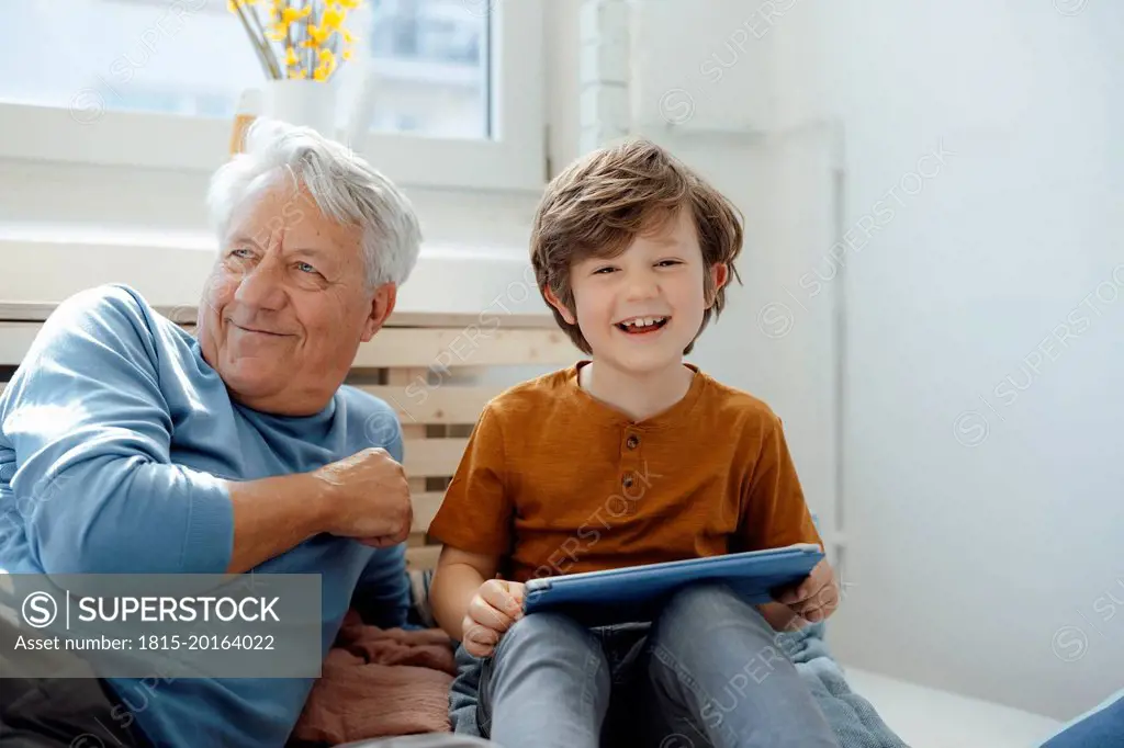 Happy boy with tablet PC sitting by grandfather at home