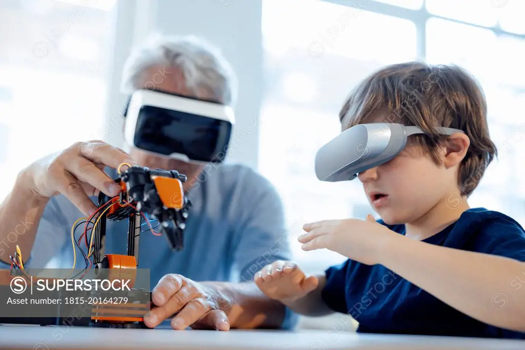 Senior man and boy with VR glasses watching robot model at home