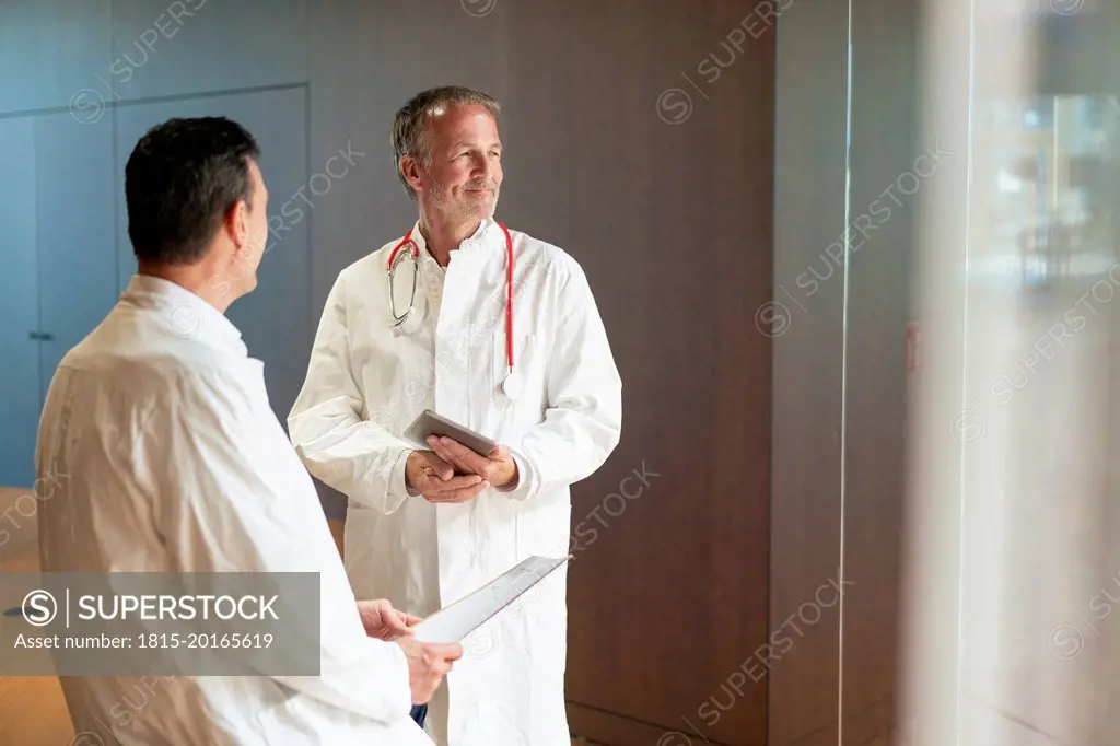 Smiling doctor holding tablet PC standing by colleague at hospital