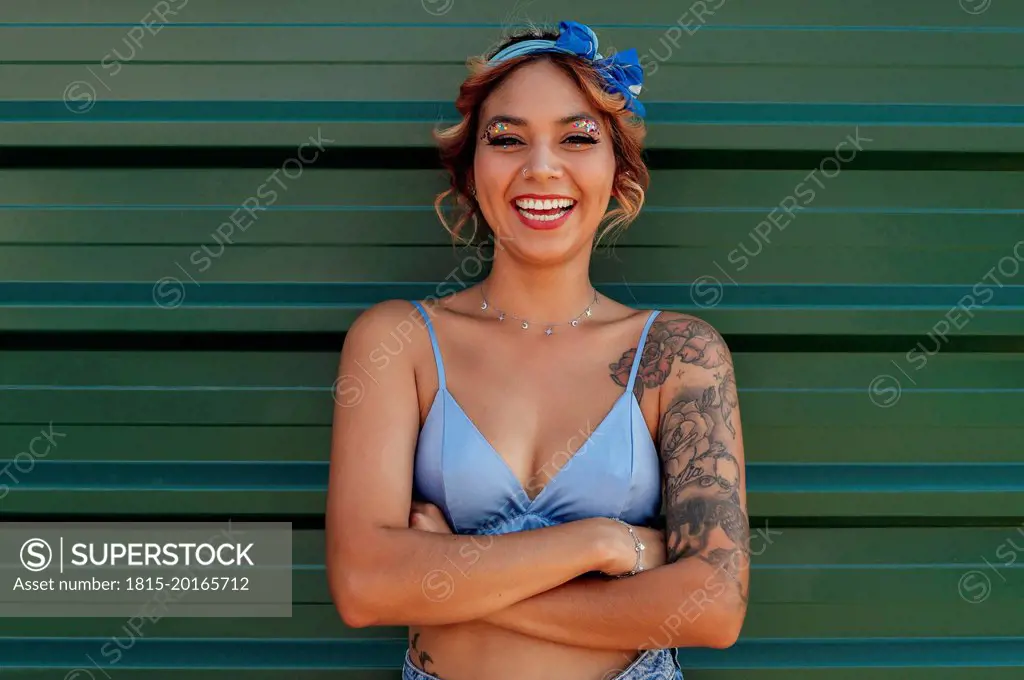 Happy woman with arms crossed standing in front of green metal wall