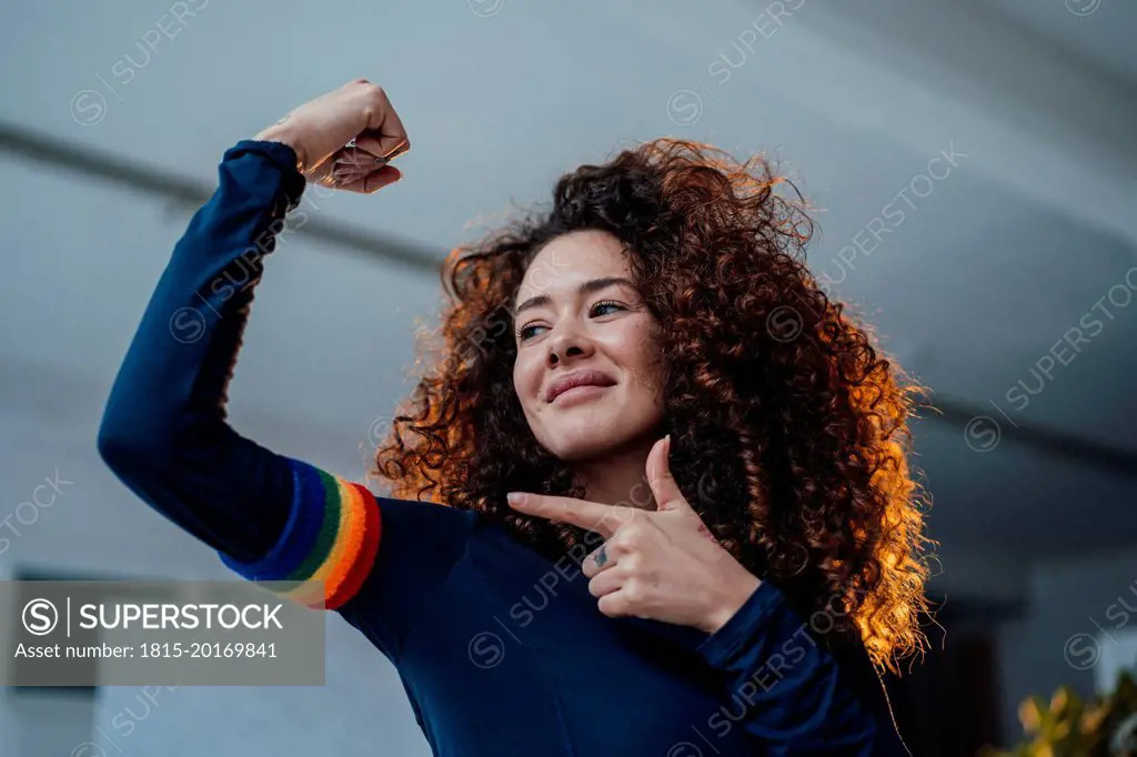 Smiling young woman flexing muscles pointing at rainbow arm band