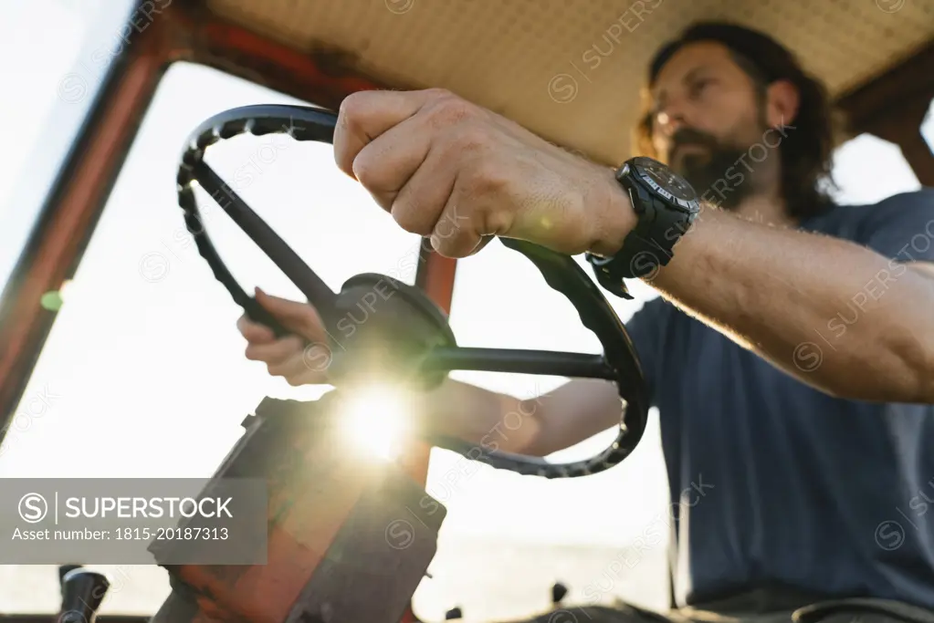 Mature farmer driving tractor on sunny day