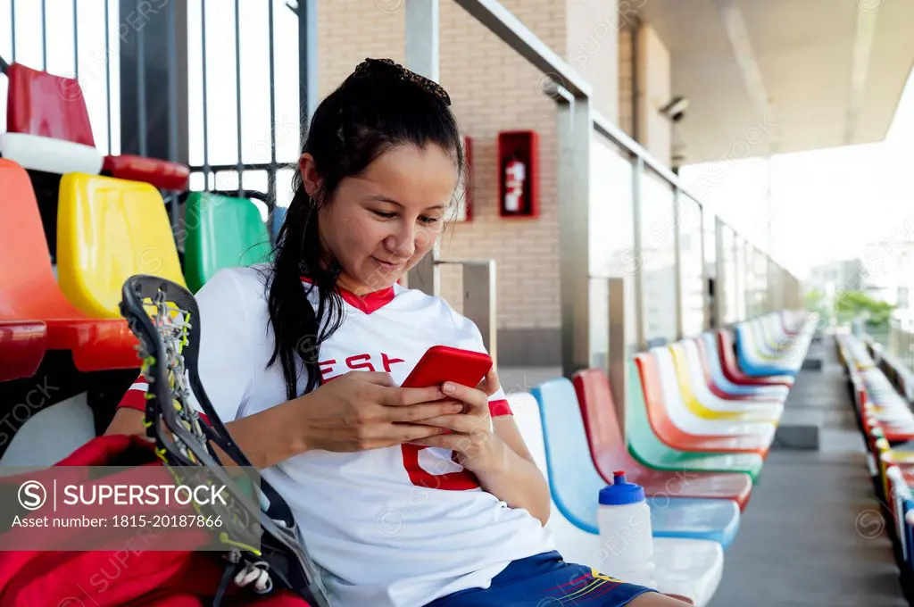 Smiling player text messaging using smart phone at stadium