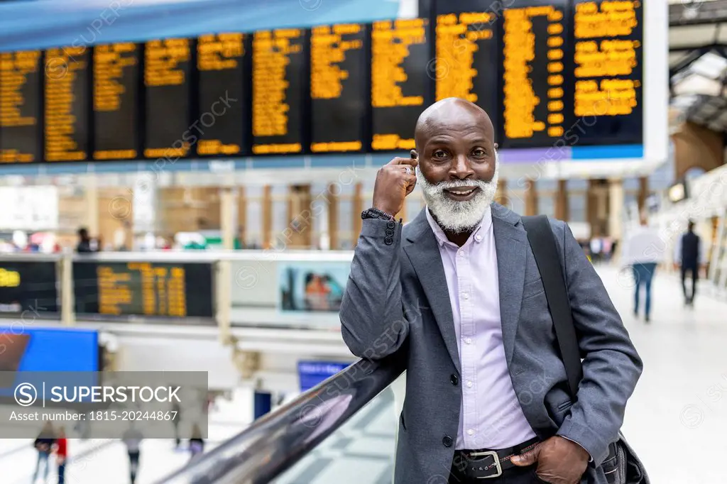 Smiling senior commuter with beard leaning on railing at railroad station