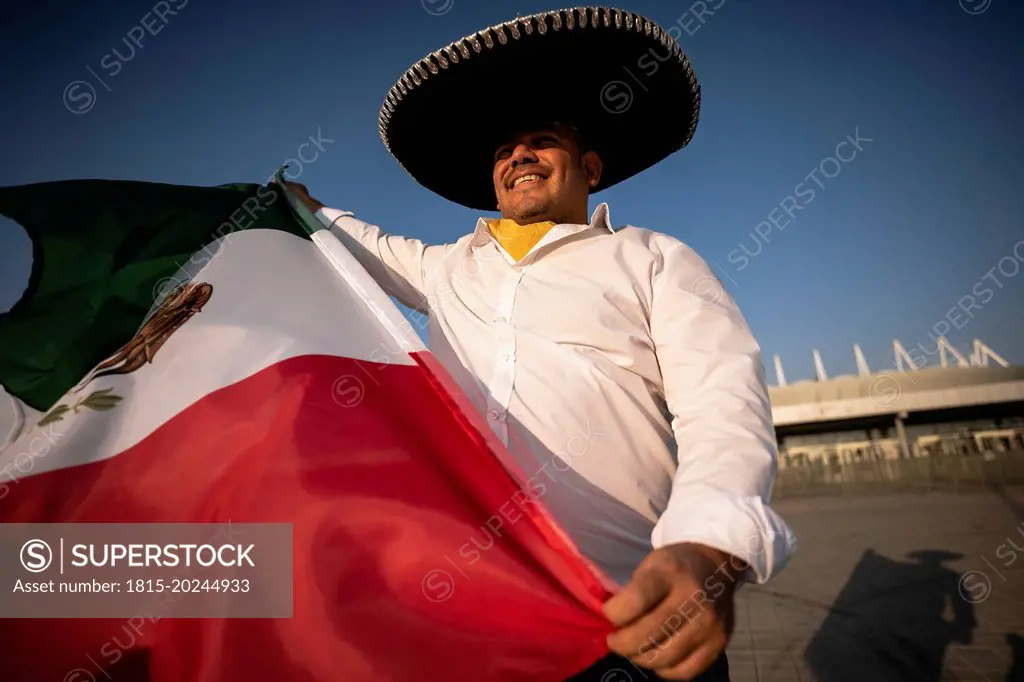 Smiling man wearing sombrero holding Mexican flag on sunny day