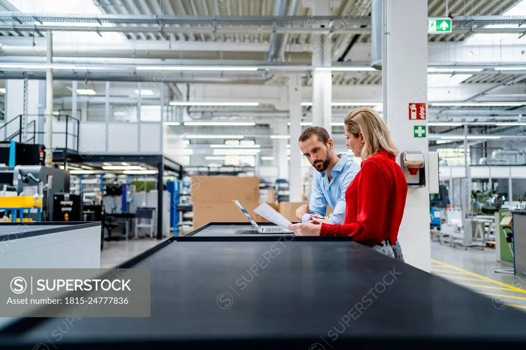 Business colleagues working on laptop at table in factory