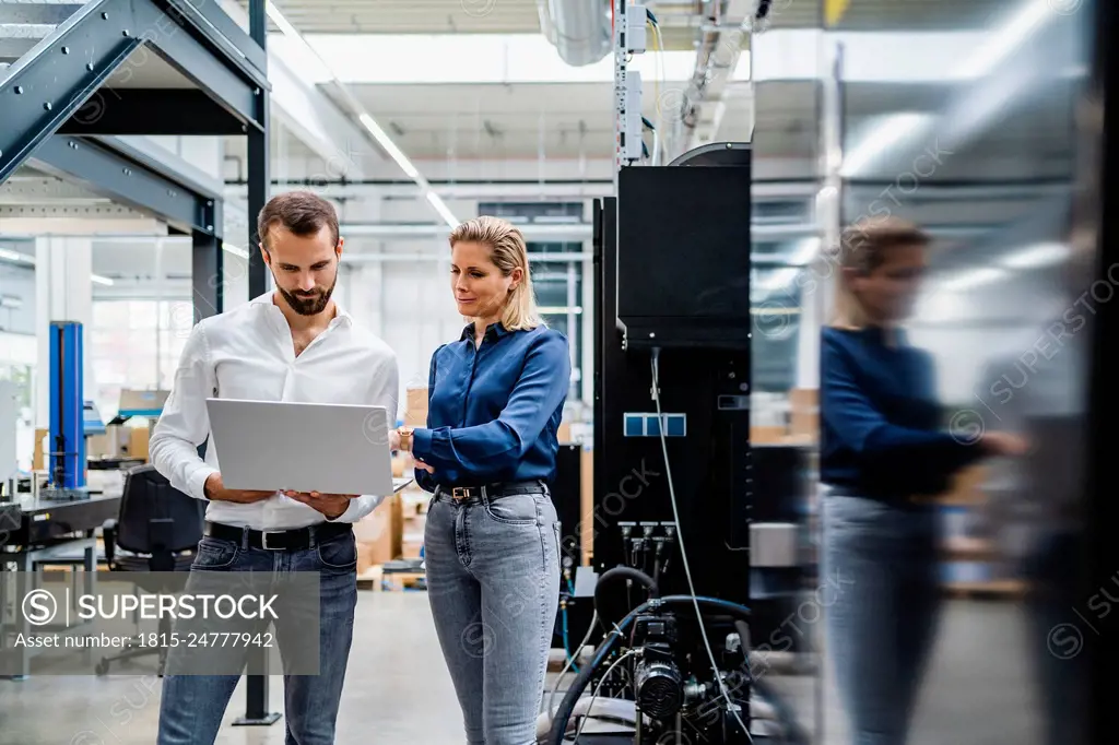 Business colleagues working on laptop standing in factory