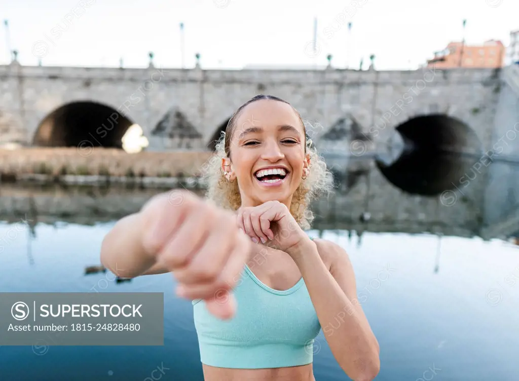 Happy sportswoman exercising and punching in front of lake