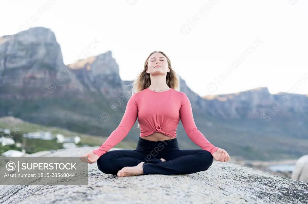 Young woman meditating on rock at beach