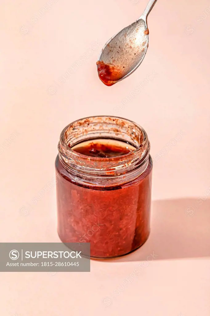 Homemade strawberry jam with spoon over peach background