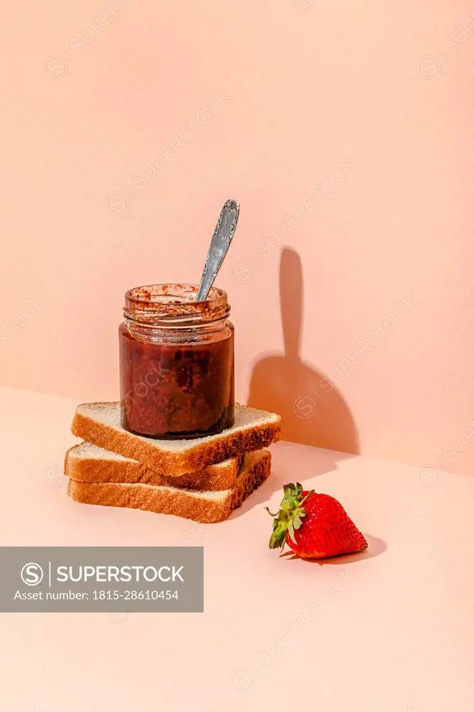 Homemade strawberry jam with slices of bread against peach background