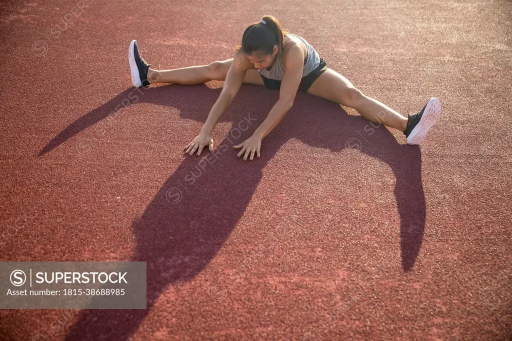 Young woman doing stretching exercise in sports field