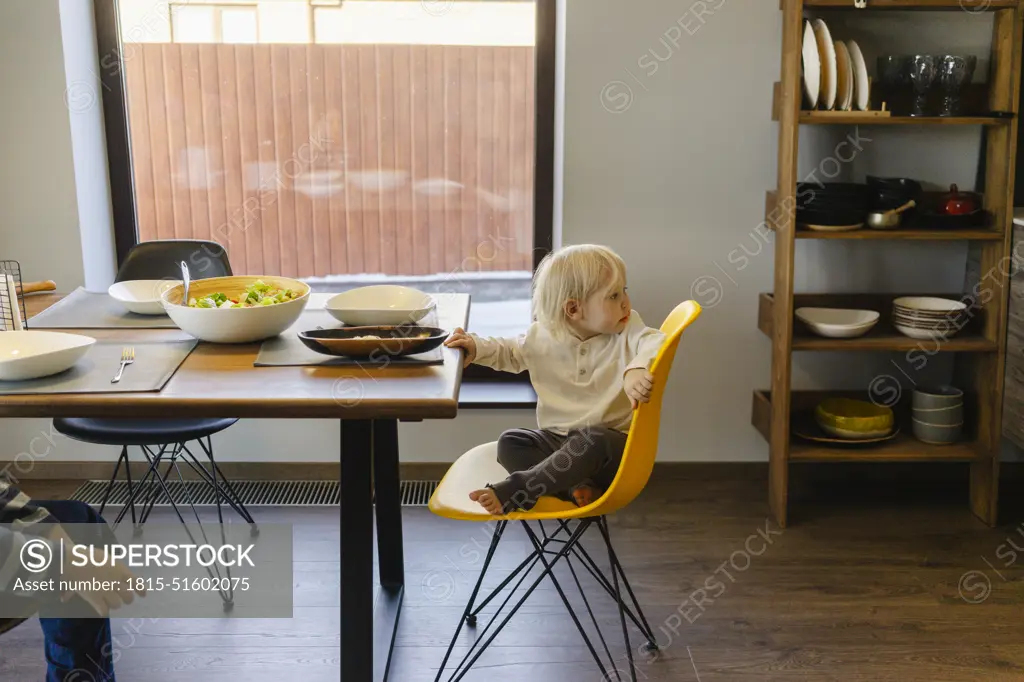 Blond girl sitting on yellow chair near dining table at home