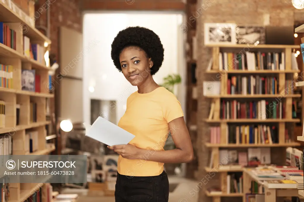 Smiling Afro woman holding book at library