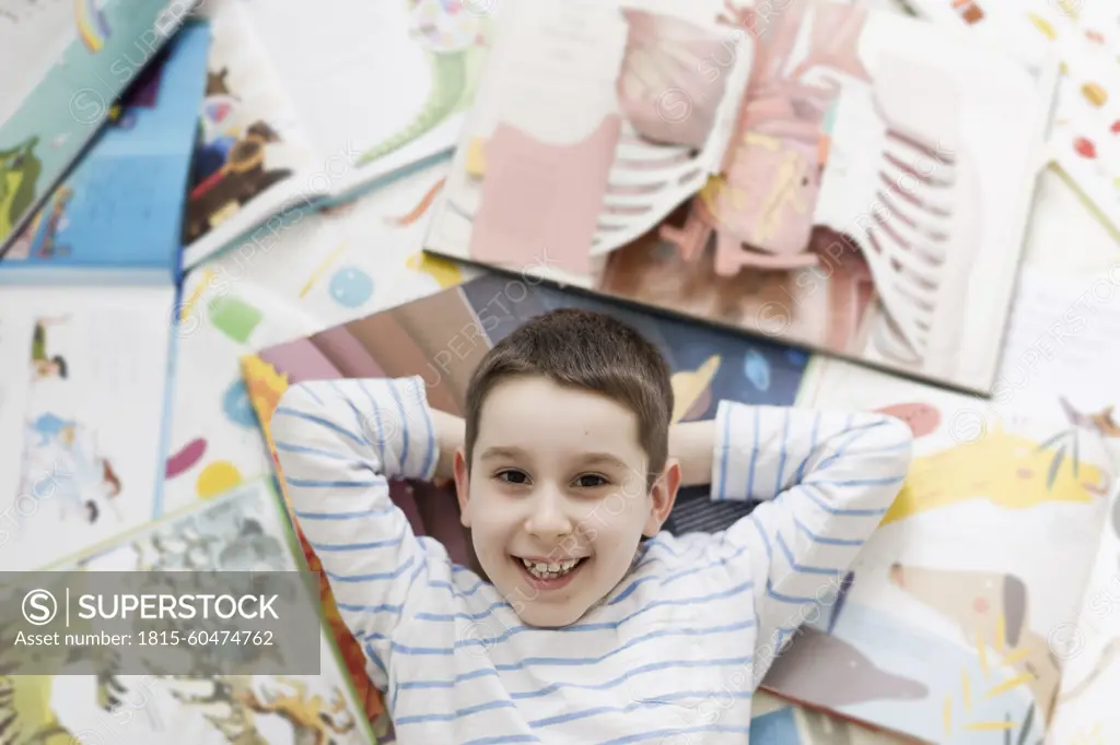 Smiling boy lying on floor amidst books at home